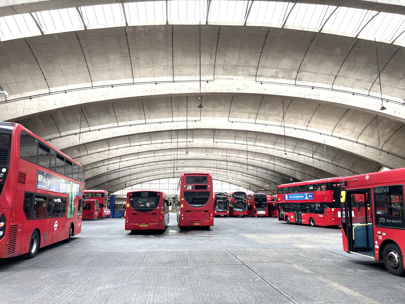 Large covered bus depot with red double-decker buses illustrating fleet scale charging requirements