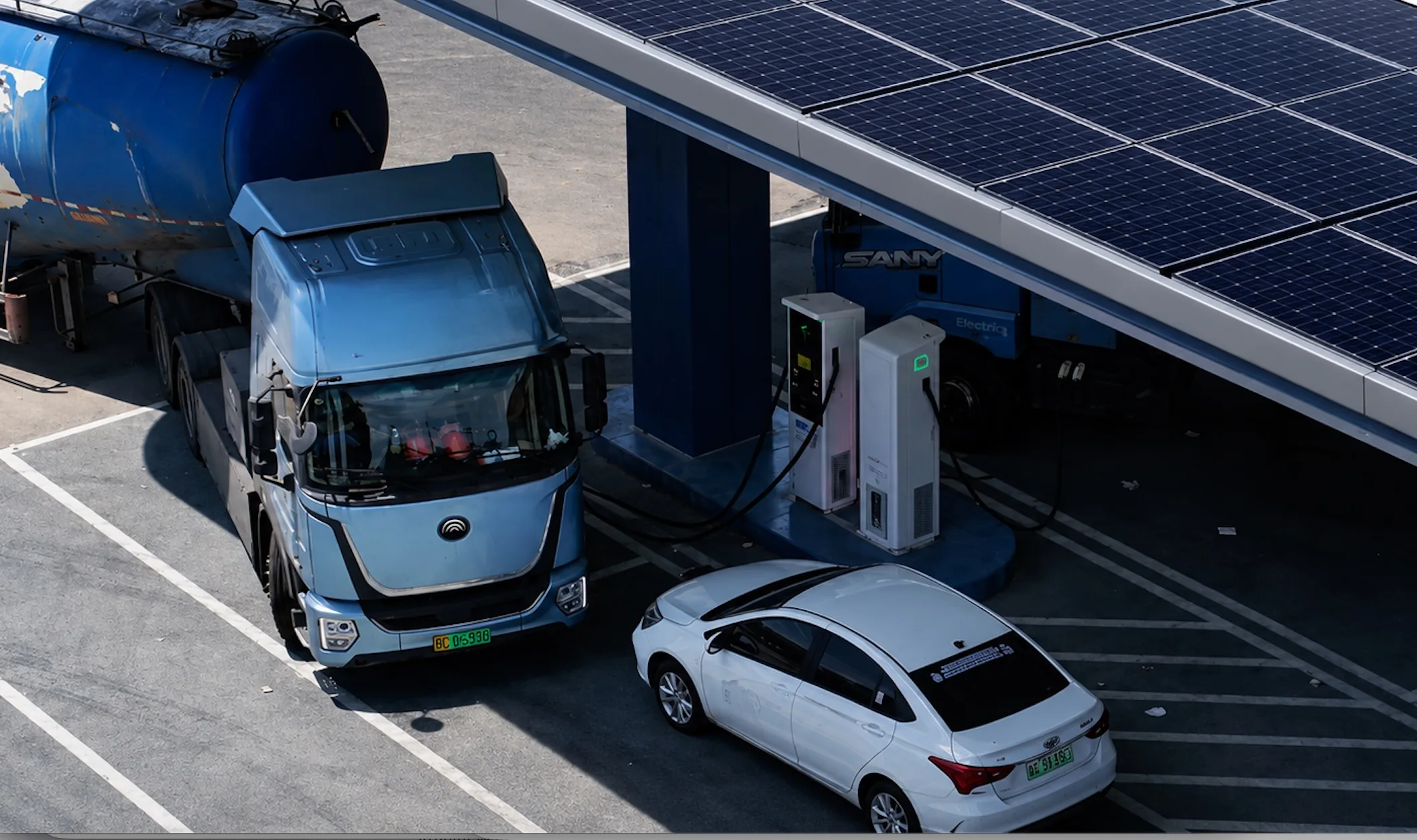 Electric HGV charging under a solar canopy at a depot site, liquid-cooled charging terminal in foreground
