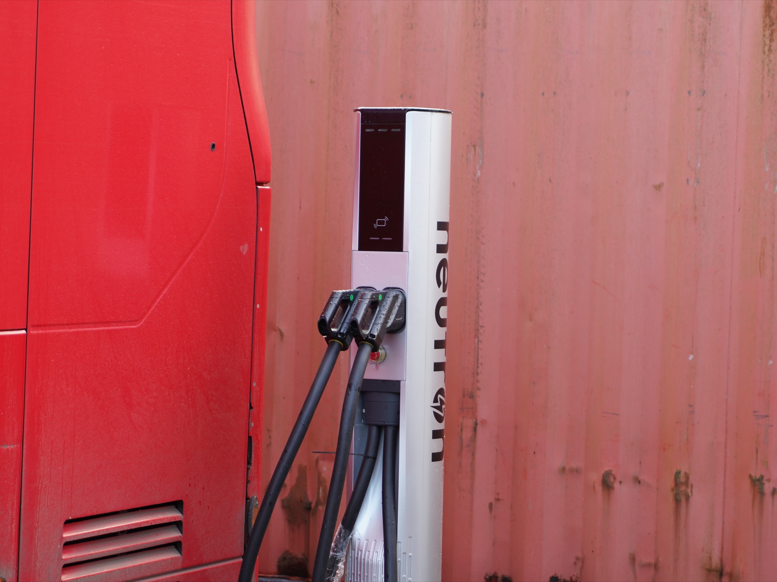 Neutron Systems satellite terminal charging a heavy goods truck with dual CCS connectors, mounted against a depot wall