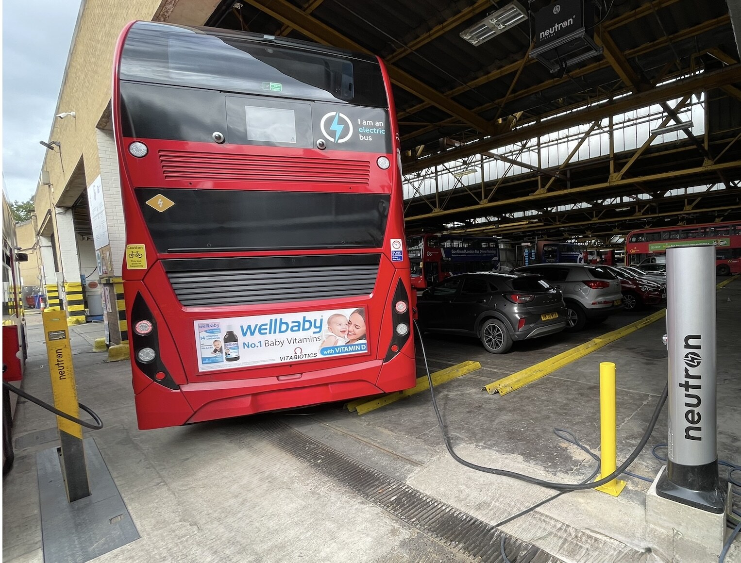 London double-decker electric bus charging via a Neutron Satellite Terminal at a London bus depot, with charging cable connected to the vehicle
